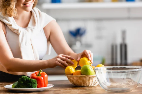 Vista recortada de la mujer tocando limones cerca de verduras en el plato - foto de stock