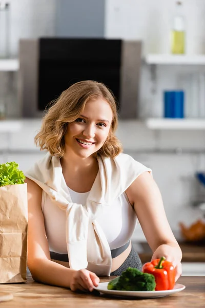 Foyer sélectif de la femme touchant plaque avec des légumes près du sac en papier — Photo de stock