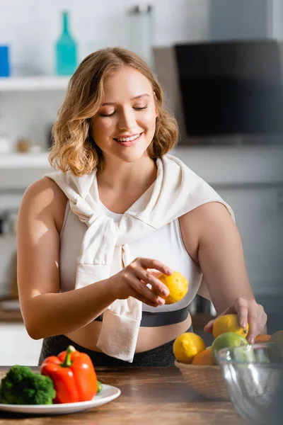Selective focus of young woman holding lemons in hands near vegetables — Stock Photo