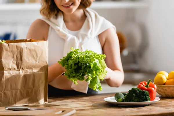 Vista recortada de la mujer sosteniendo lechuga cerca de verduras en el plato - foto de stock