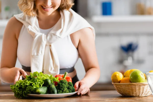 Cropped view of woman touching plate with vegetables near lemons — Stock Photo