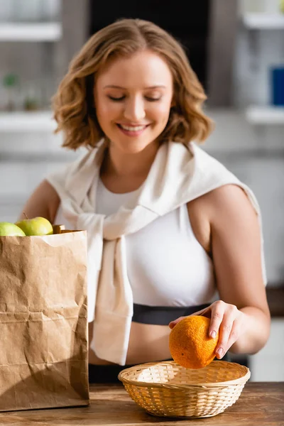 Enfoque selectivo de la mujer sosteniendo naranja cerca de la bolsa de papel con frutas - foto de stock