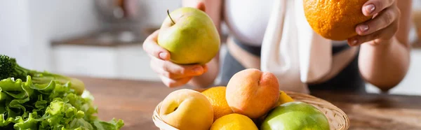 Horizontal crop of woman holding orange and apple in hands — Stock Photo