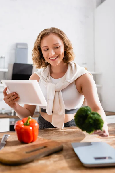 Foco seletivo da mulher segurando tablet digital e brócolis na cozinha — Fotografia de Stock