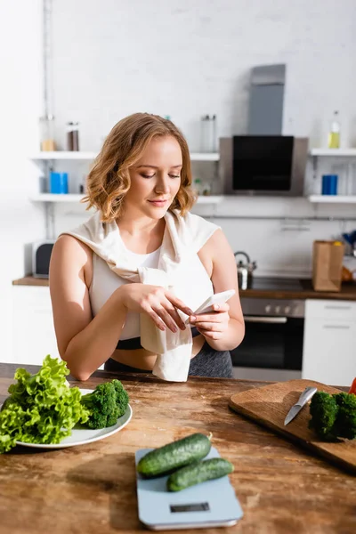 Selective focus of woman using smartphone near green vegetables — Stock Photo