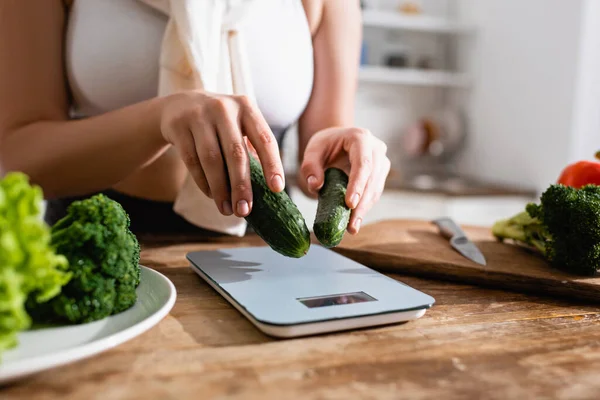 Vista recortada de la mujer poniendo pepinos en las escalas de la cocina - foto de stock