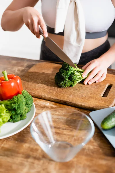 Vista ritagliata di donna che taglia broccoli freschi sul tagliere vicino alle verdure — Foto stock