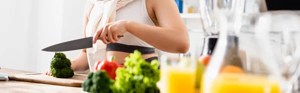 Frau schneidet frischen Brokkoli auf Schneidebrett in der Nähe von Krug mit Orangensaft — Stockfoto