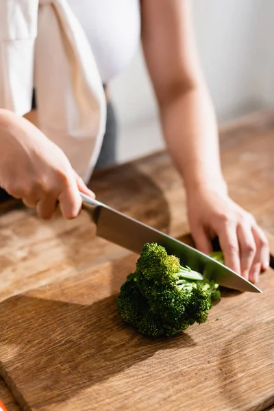 Cropped view of woman cutting fresh broccoli on chopping board — Stock Photo