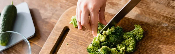 Culture panoramique de femme coupant brocoli frais sur planche à découper près des balances de cuisine avec concombre — Photo de stock