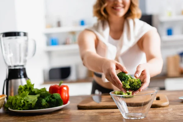 Cropped view of woman putting broccoli in bowl near vegetables — Stock Photo