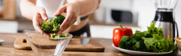 Orientación panorámica de la mujer poniendo brócoli en un tazón cerca de las verduras - foto de stock