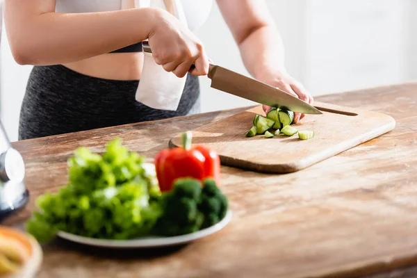 Cropped view of young woman cutting cucumber on chopping board — Stock Photo