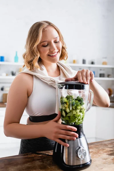 Junge Frau berührt Mixer mit geschnittenem Salat und Gurke — Stockfoto