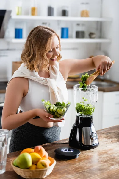 Selektiver Fokus der Frau, die frischen Salat im Mixer hinzufügt — Stockfoto