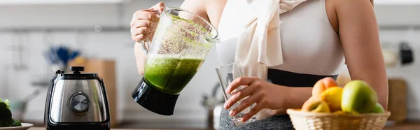 Panoramic crop of young woman holding blender with mixed smoothie near glass — Stock Photo