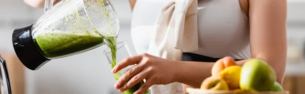 Imagem horizontal da jovem mulher derramando smoothie verde misto em vidro — Fotografia de Stock