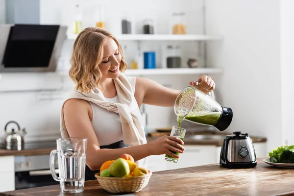 Foyer sélectif de la femme versant smoothie vert dans le verre près des fruits — Photo de stock