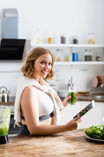 Избирательный фокус молодой женщины, держащей стакан зеленого смузи и цифровой планшет с чистым экраном — стоковое фото