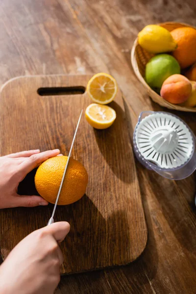 Vista cortada de mulher cortando laranja perto de juicer — Fotografia de Stock