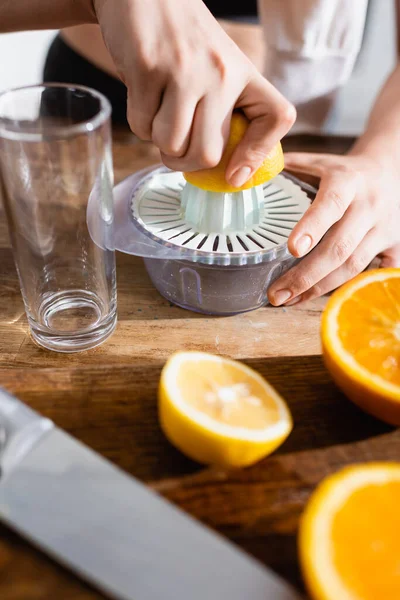 Vista cortada de mulher jovem espremendo metade de laranja no espremedor — Fotografia de Stock