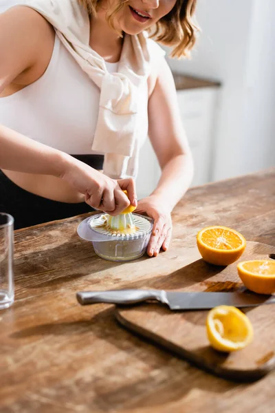 Vista recortada de la joven mujer exprimiendo naranja mientras prepara jugo - foto de stock