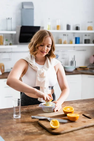 Foco seletivo de mulher jovem espremendo laranja enquanto prepara suco na cozinha — Stock Photo