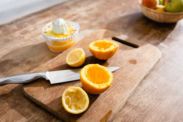Selective focus of squeezed orange halves near knife and juicer — Stock Photo
