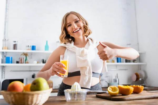 Selective focus of woman showing thumb up and holding glass with fresh orange juice — Stock Photo