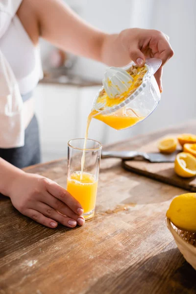 Обрезанный вид женщины, наливающей свежий апельсиновый сок в стакан рядом с сжатыми фруктами — стоковое фото