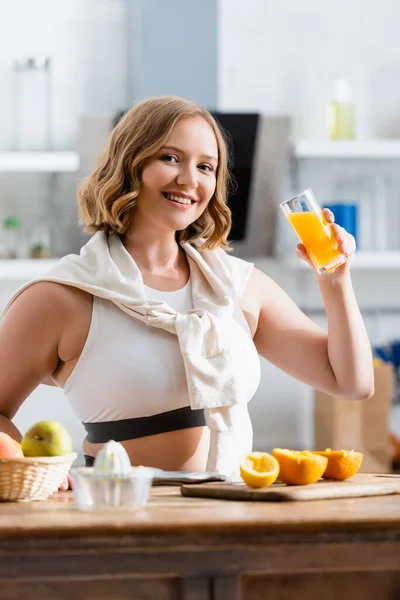 Жінка тримає скло зі свіжим апельсиновим соком і дивиться на камеру — стокове фото