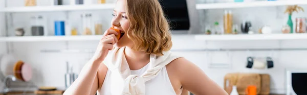 Panoramic crop of woman eating fresh peach in kitchen — Stock Photo