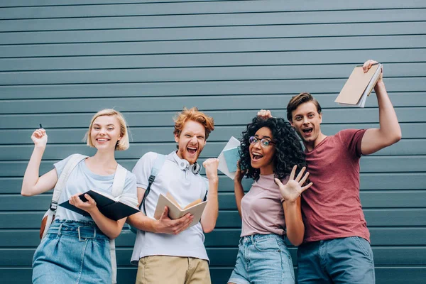 Aufgeregte multiethnische Studenten zeigen Siegergeste, während sie Bücher über urbanes Sreet in der Hand halten — Stockfoto