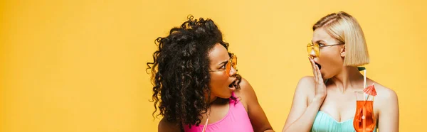 Concetto panoramico di donna bionda scioccata in possesso di bicchiere da cocktail e bocca di copertura con mano vicino amico afro-americano — Foto stock