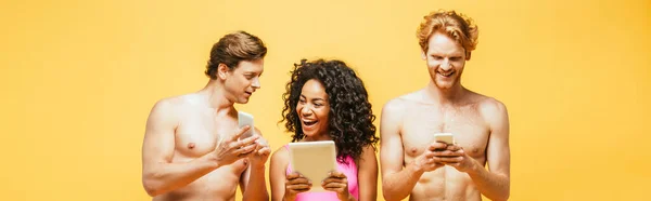 Imagen horizontal de la mujer afroamericana y los hombres sin camisa utilizando dispositivos digitales aislados en amarillo - foto de stock