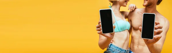 Vista recortada de hombre y mujer sin camisa en sujetador de natación mostrando teléfonos inteligentes con pantalla en blanco aislado en amarillo, imagen horizontal - foto de stock