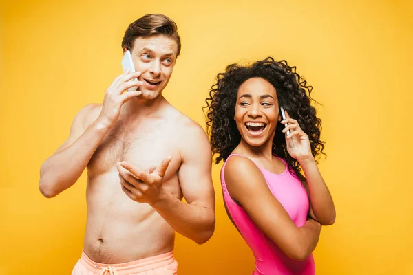 African american woman in swimsuit and shirtless man talking on smartphones on yellow — Stock Photo
