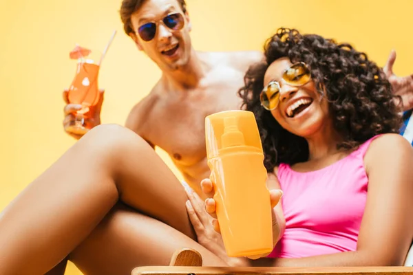 Jovem casal interracial com suco de laranja e coquetel olhando para a câmera isolada no amarelo — Fotografia de Stock