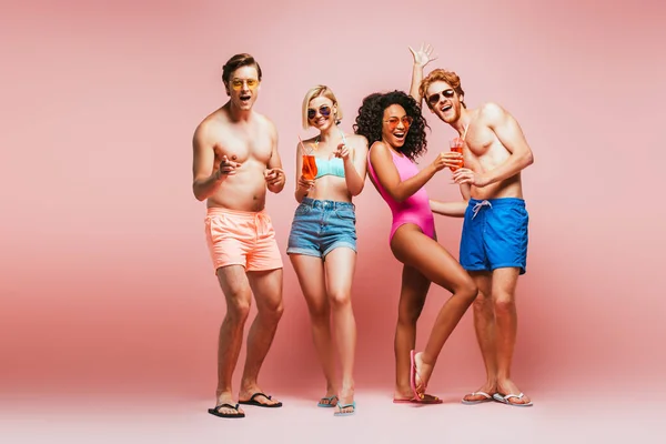 Full length view of excited african american girl standing with raised hand near multicultural friends with cocktail glasses isolated on pink — Stock Photo