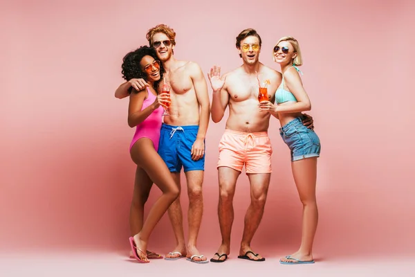 Shirtless man waving hand while looking at camera together with multicultural friends holding cocktails isolated on pink — Stock Photo