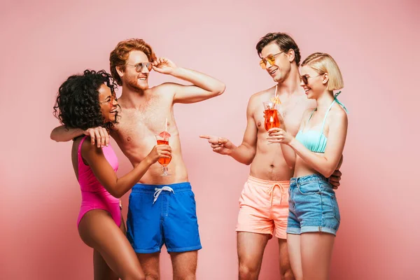 Без сорочки чоловік вказує пальцем біля мультикультурних друзів тримає коктейлі ізольовані на рожевому — стокове фото
