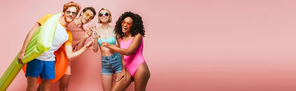Website header of young multicultural friends looking at camera and clinking champagne glasses on pink — Stock Photo