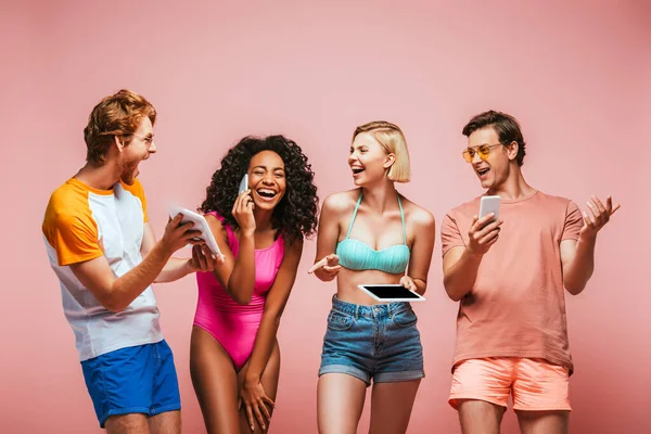 Excited africal american woman talking on smartphone near multicultural friends using gadgets isolated on pink — Stock Photo