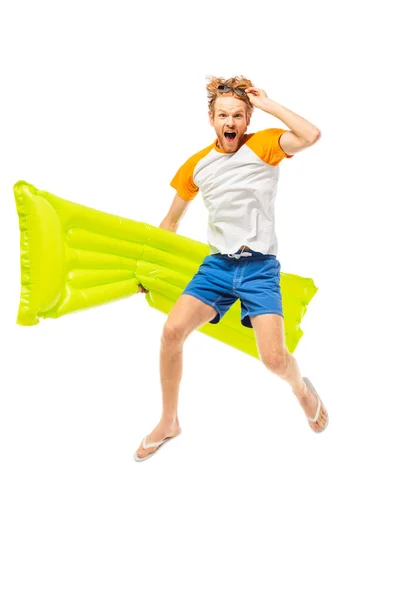 Excited man holding sunglasses and inflatable mattress while jumping isolated on white — Stock Photo