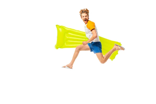 Vista lateral del hombre excitado sosteniendo el colchón inflable mientras que salta aislado en blanco - foto de stock