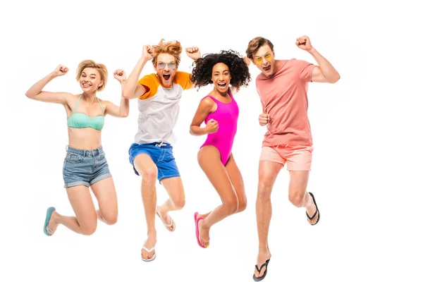 Multiethnic friends in sunglasses and swimsuits showing yeah gesture while jumping isolated on white — Stock Photo