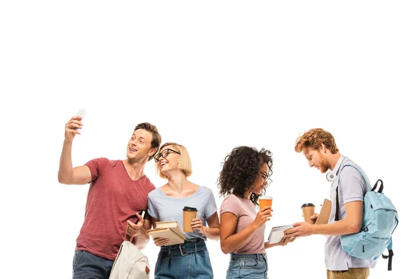Multicultural students with coffee to go taking selfie and holding books isolated on white — Stock Photo