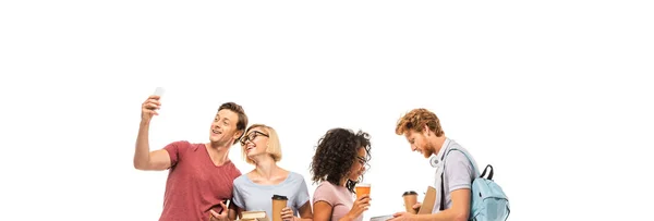 Panoramic shot of multiethnic students taking selfie and holding books with coffee to go isolated on white — Stock Photo