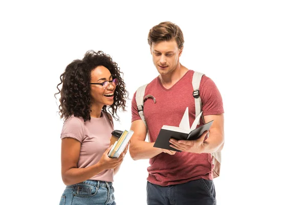 Studente in possesso di notebook vicino amico afro-americano con caffè per andare e libri isolati su bianco — Foto stock