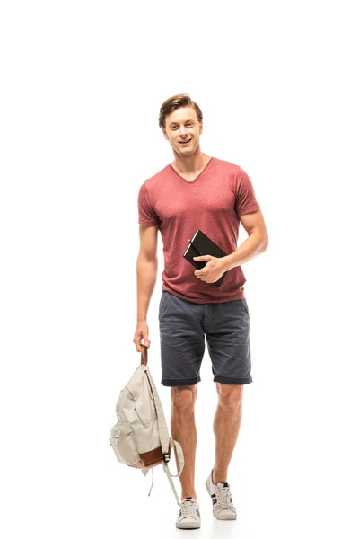 Student hält Rucksack und Notizbuch in der Hand, während er auf weißem Hintergrund in die Kamera blickt — Stockfoto